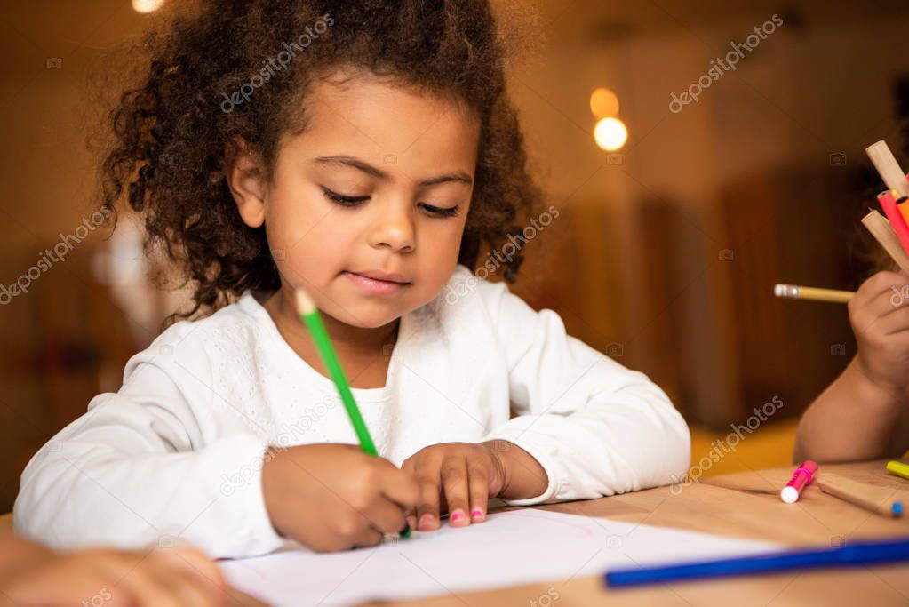 adorable african american kid erasing pencil from sheet of paper in kindergarten