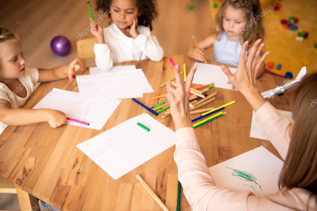 educator showing number seven with fingers to multicultural kids in kindergarten