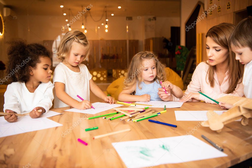 educator drawing together with multicultural kids in kindergarten