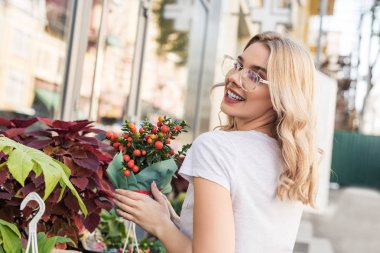 smiling attractive florist holding potted plant near flower shop clipart