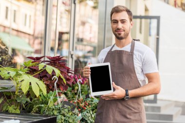 Tablet boş ekran ile çiçek dükkan yakın tutarak ve kameraya bakarak yakışıklı çiçekçi