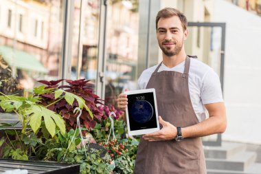 iPad çiçek dükkan yakın tutarak ve kameraya bakarak yakışıklı çiçekçi