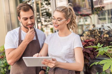 smiling florists looking at tablet near flower shop clipart