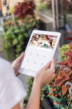 Çiçekçi çiçekçi dükkanı yakınındaki yüklü oturaklı sayfayla tablet kullanarak kırpılmış görüntü