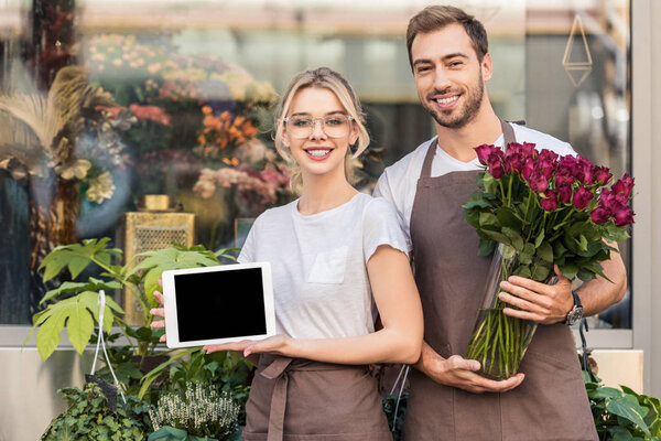 happy florists holding tablet with blank screen and burgundy roses near flower shop