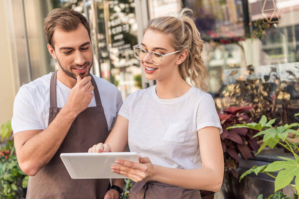 smiling florists looking at tablet near flower shop