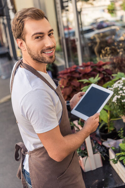 smiling handsome florist holding tablet with blank screen near flower shop