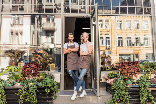 smiling female and male florists standing in open door of flower shop