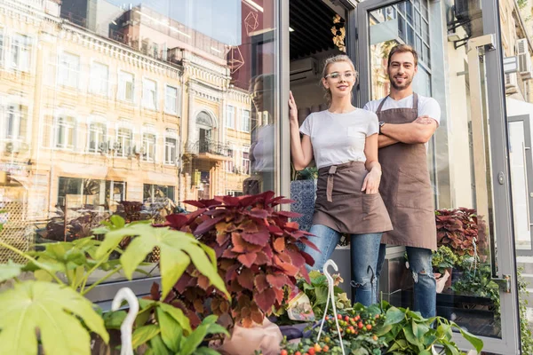 smiling colleagues standing near flower shop and looking at camera