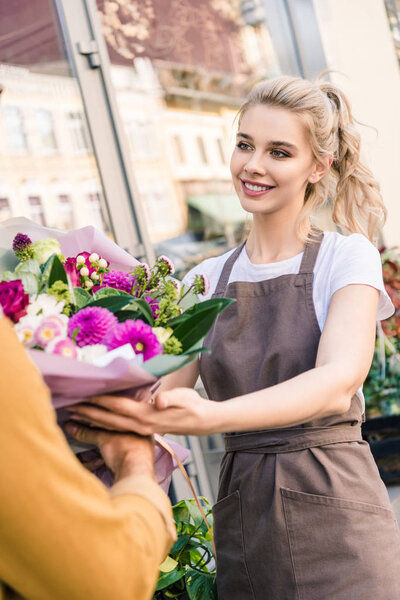 smiling attractive florist giving beautiful bouquet of chrysanthemums to customer near flower shop