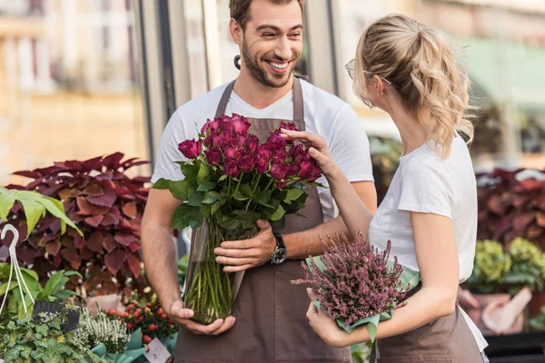 Smiling florists talking and standing near flower shop with potted plant and burgundy roses — Stock Image Smiling Florists Talking Standing Flower Shop Potted Plant Burgundy Roses Stock Image