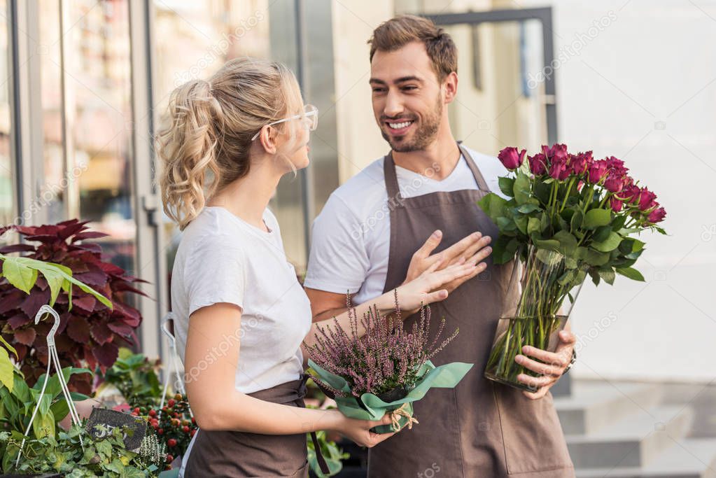 happy colleagues talking and standing near flower shop with potted plant and burgundy roses
