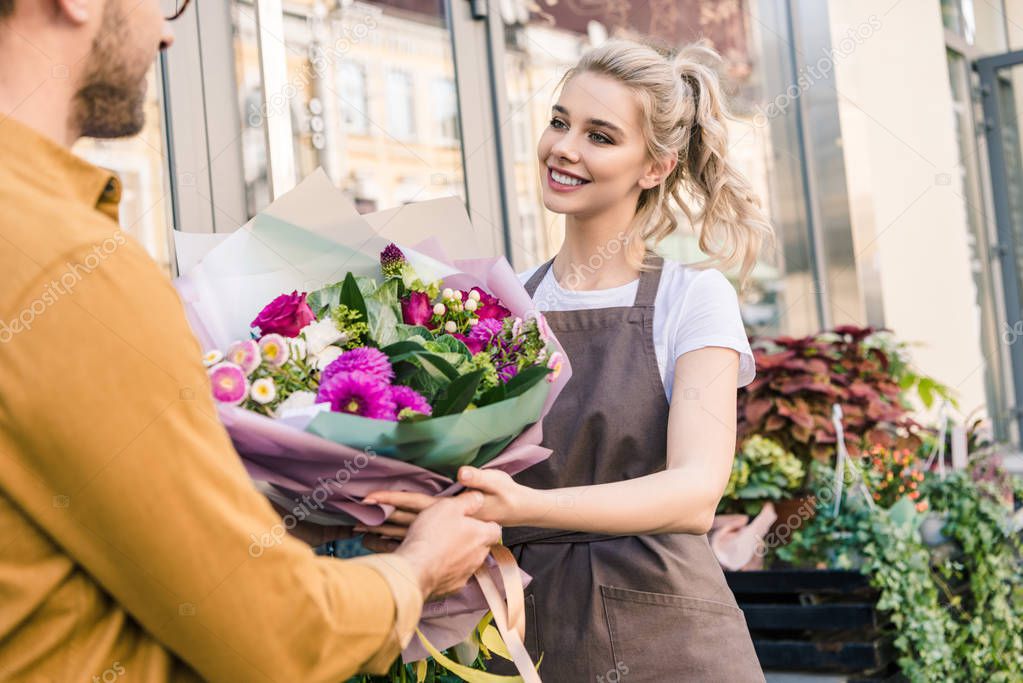 smiling florist giving beautiful bouquet of chrysanthemums to customer near flower shop