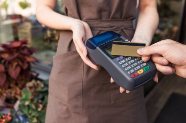 cropped image of customer paying with credit card at flower shop, florist holding payment terminal clipart