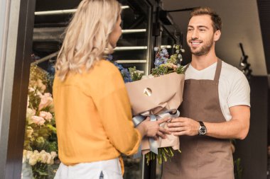 handsome florist giving wrapped bouquet to customer at flower shop clipart