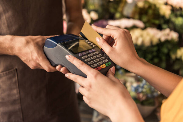 cropped image of female customer paying with credit card at flower shop, florist holding pos terminal
