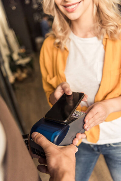 cropped image of smiling customer making contactless payment with smartphone at flower shop