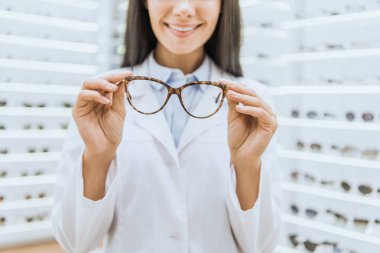 Gözlük tutan gülümseyen profesyonel optometrist kırpılmış görünümünü