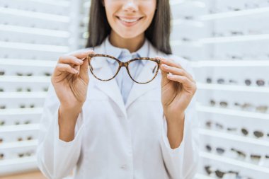 cropped view of smiling professional optometrist holding glasses clipart