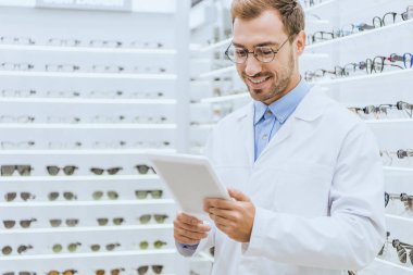 Erkek gözlükçü optica raflar gözlük ile dijital tablet kullanarak gülümseyen