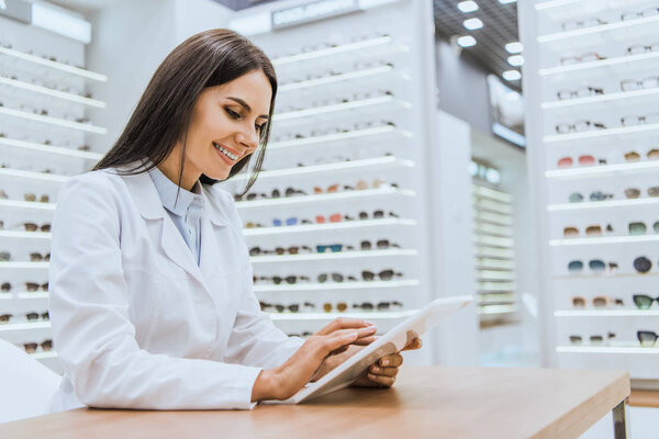 smiling doctor using digital tablet in ophthalmic shop