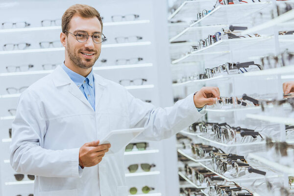 professional optometrist with digital tablet taking eyeglasses from shelves in optica