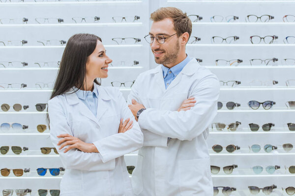 happy professional opticians in white coats posing with crossed arms in ophthalmology