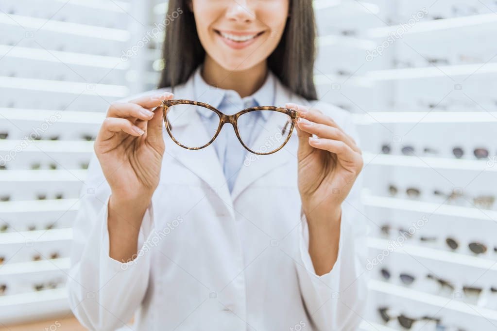 cropped view of smiling professional optometrist holding glasses