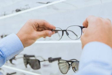 cropped view of person taking eyeglasses from shelf in optica clipart