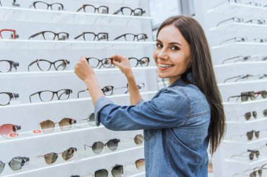 güzel genç kadın optica içinde gözlük raflardan alarak