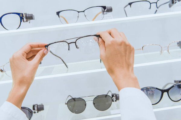cropped view of doctor taking eyeglasses from shelf in ophthalmic shop