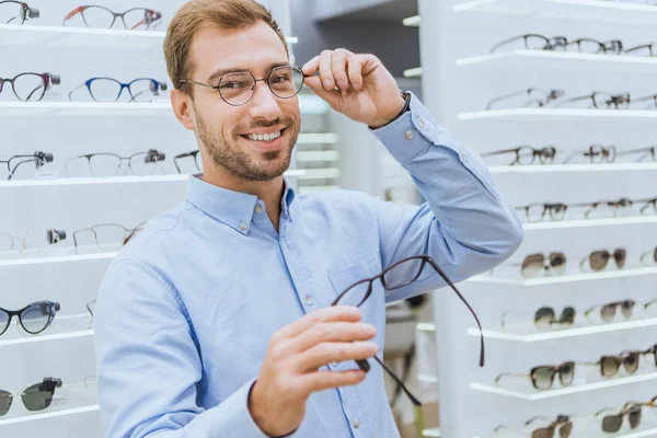 Fröhlicher Junger Mann Wählt Brille Und Blickt Augenarztpraxis Die Kamera — Stockfoto