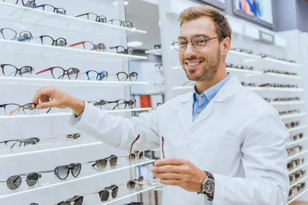 Optician Sorrindo Revestimento Branco Que Toma Vista Das Prateleiras Oftalmologia — Fotografia de Stock Grátis