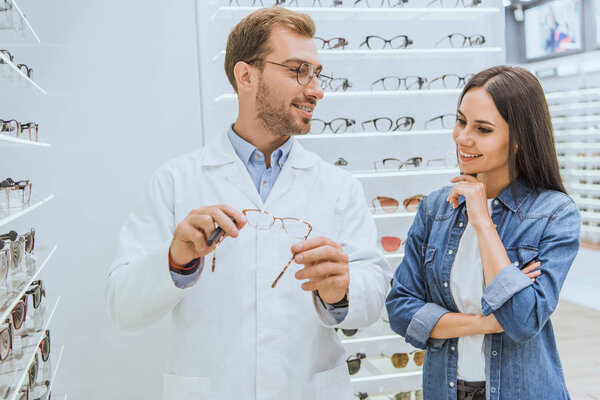 male optometrist showing eyeglasses to smiling woman in optica 