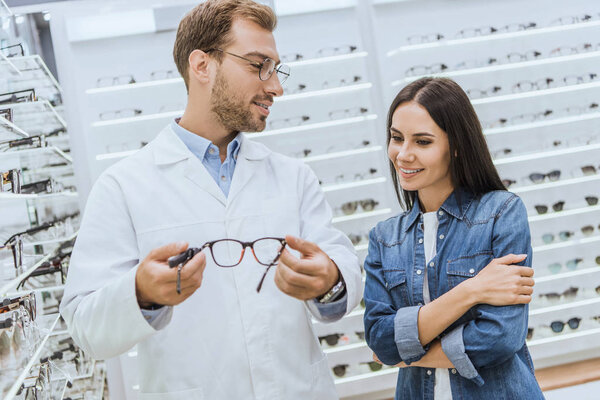 male optometrist showing eyeglasses to young woman in ophthalmic shop