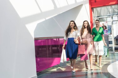şık kağıt torba tutarak ve birlikte alışveriş merkezinde yürüyen genç kadın gülümseyerek