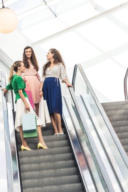 kağıt torbalar alışveriş alışveriş merkezinde yürüyen merdiven üzerinde tutan güzel gülümseyen genç kadınların düşük açılı görünüş