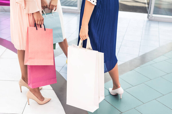 обрезанный снимок стильных девушек, держащих бумажные пакеты в торговом центре
