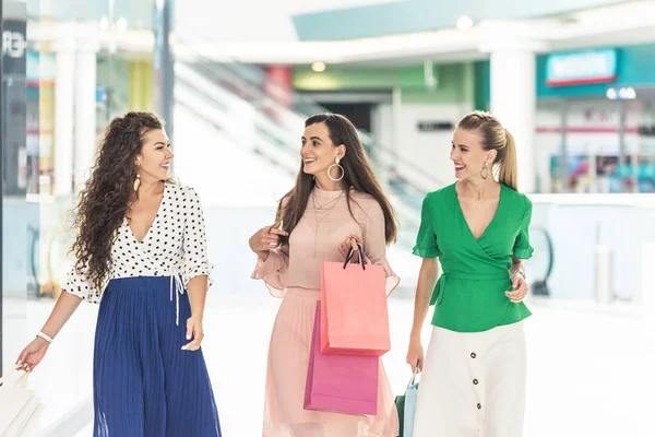 Sonrientes Mujeres Jóvenes Sosteniendo Bolsas Papel Hablando Mientras Caminan Juntas —  Fotos de Stock