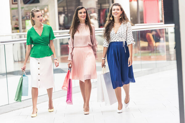 beautiful smiling fashionable girls with paper bags walking in shopping mall