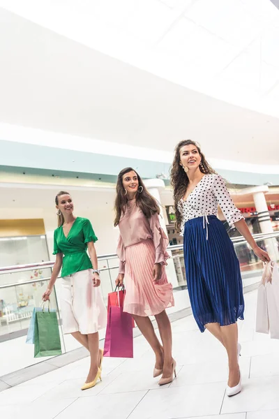 微笑的年轻妇女拿着纸袋 看着走在一起在购物中心 — 免费的图库照片