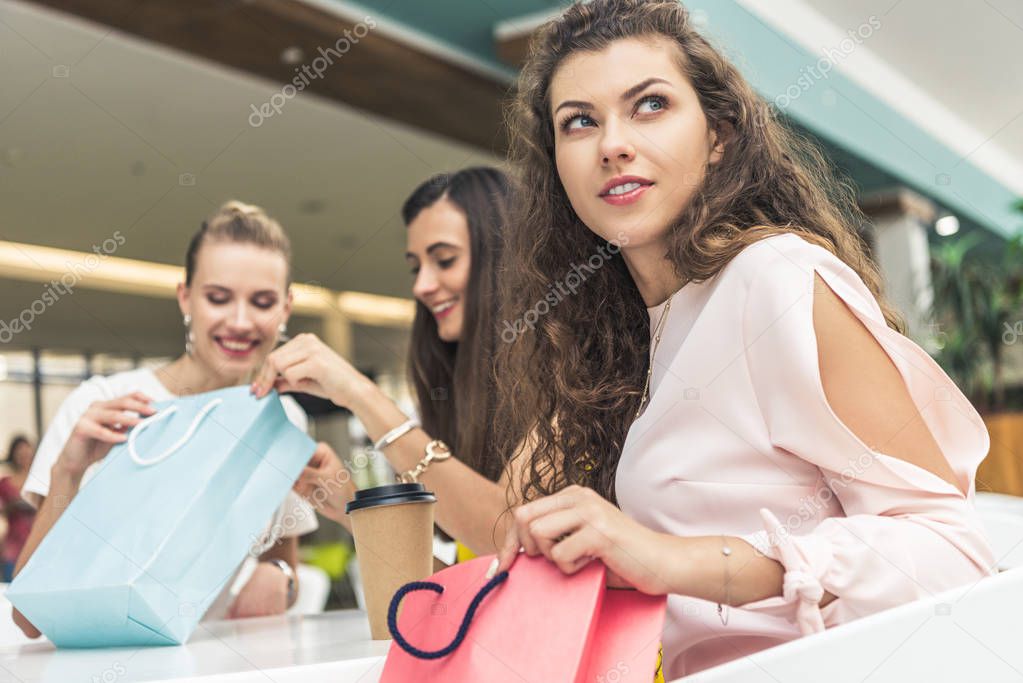 beautiful young women looking into paper bags while sitting in cafe at shopping mall