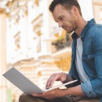 Beau jeune homme travaillant avec ordinateur portable dans la rue