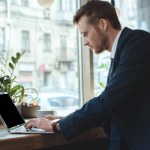 Zijaanzicht van geconcentreerde zakenman die op laptop aan tafel met een kopje koffie in het restaurant werkt