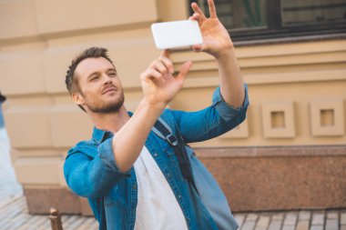attractive young tourist with backpack taking photo with smartphone on street clipart