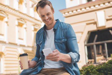 mutlu genç adam kahve ile Smartphone sokakta kullanmaya devam