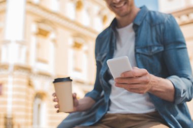 Genç adam kahve ile smartphone sokakta kullanmaya devam gülümseyen in kırpılmış atış
