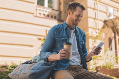 Kağıt bardak kahve sokakta smartphone kullanarak ile yakışıklı genç
