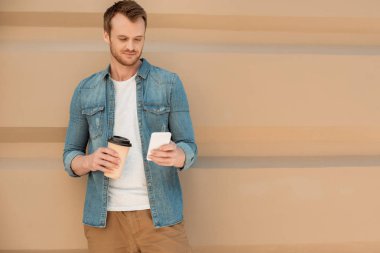 mutlu genç adam kahve ile Smartphone duvar önünde kullanmaya devam