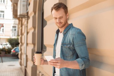yakışıklı genç adam kahve ile Smartphone sokakta kullanmaya devam